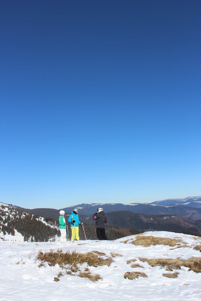 about-01 Three skiers pause on a snow-covered mountain with a stunning view under a clear blue sky.